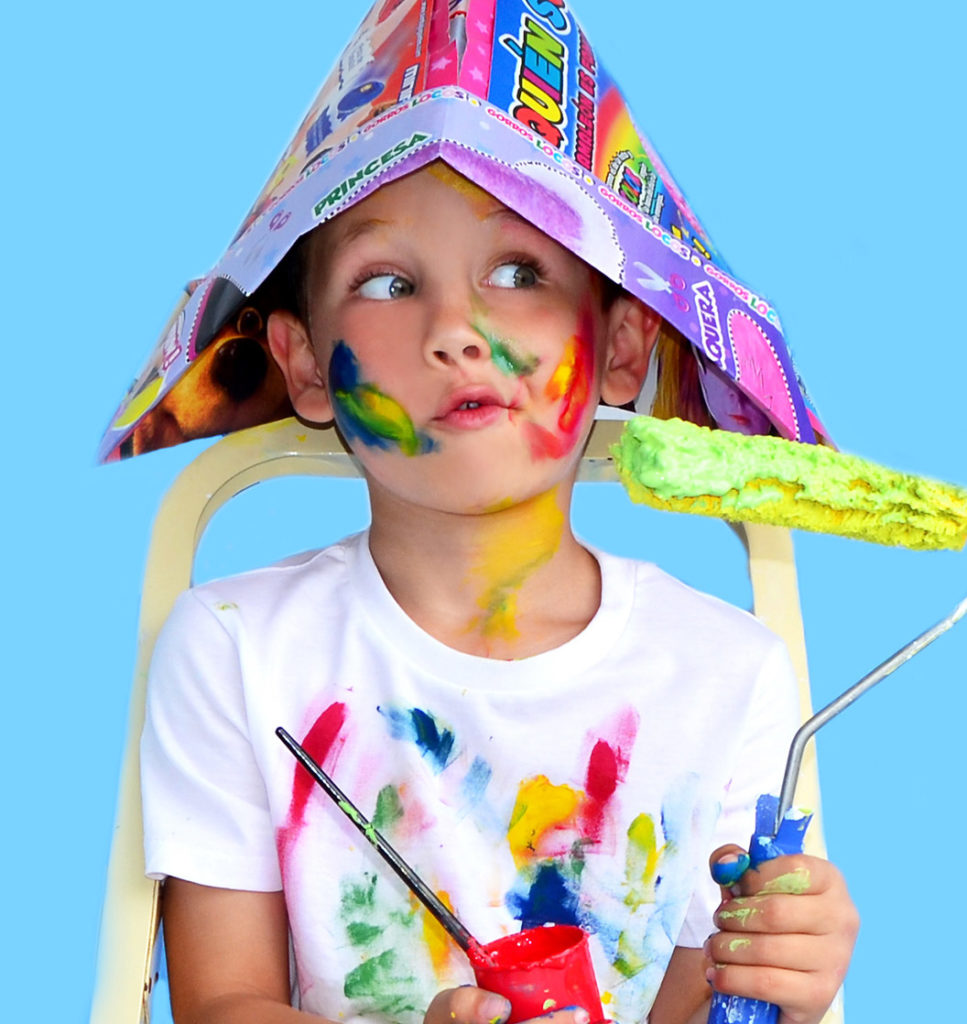 an image of a young boy with paint all over his face, hands, and shirt, sitting in front of a light blue backdrop